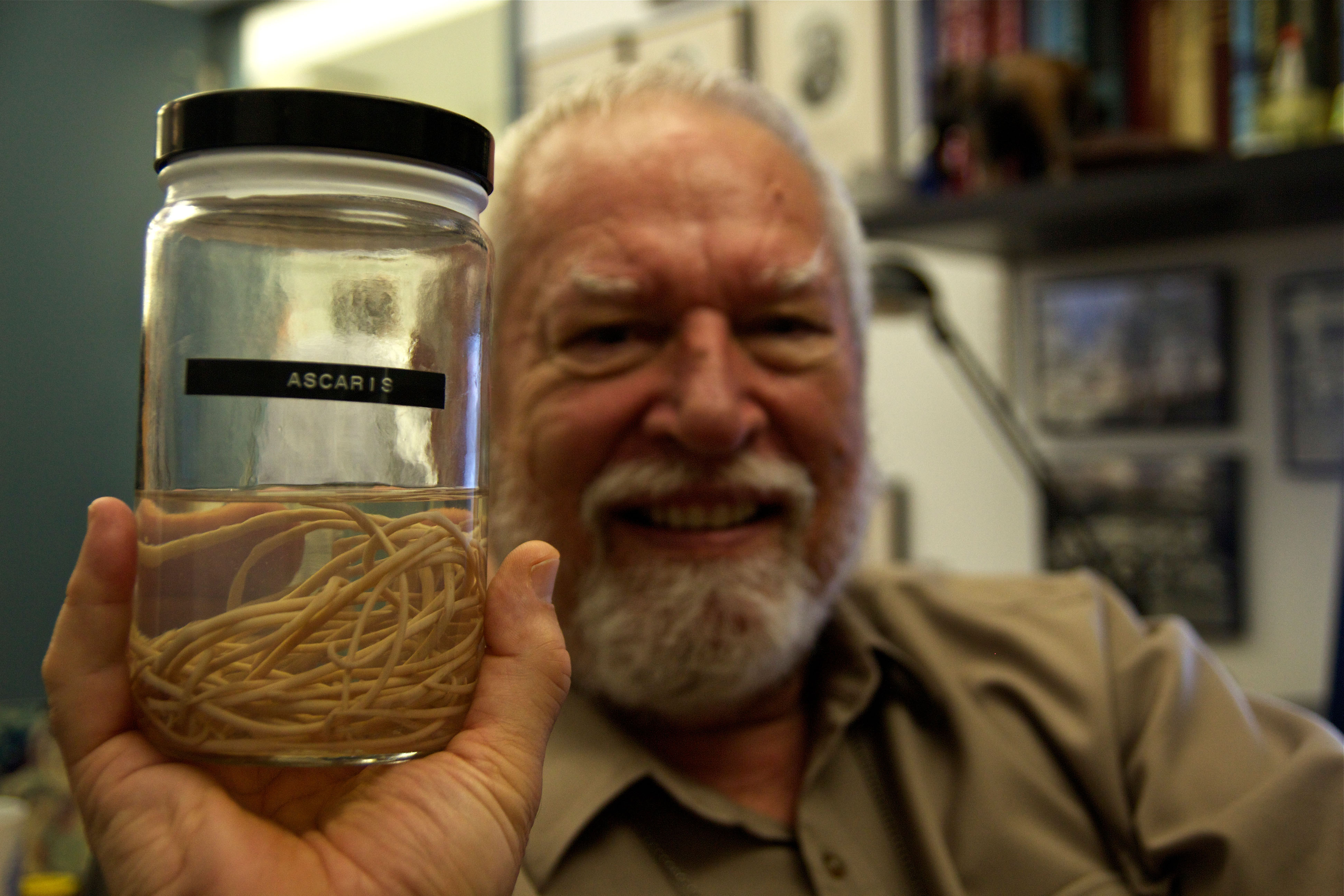 A scientistic with a beard holds a jar with ascaris parasite